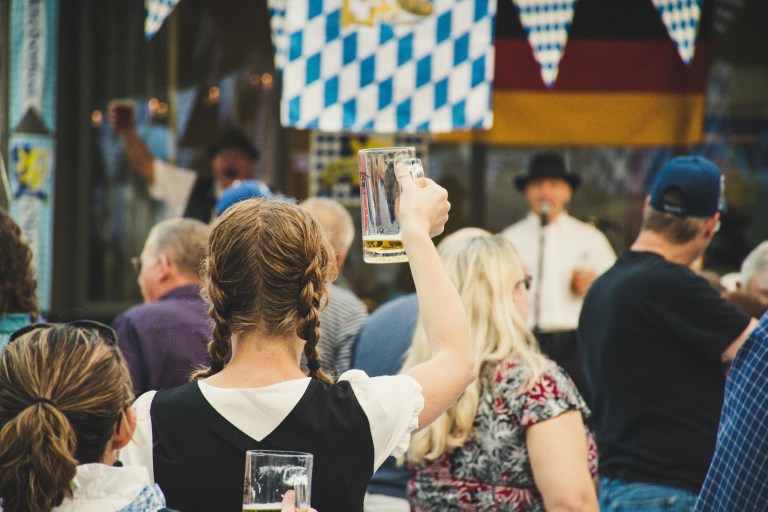Woman in braids raises beer mug at crowded festival with flags and performer.