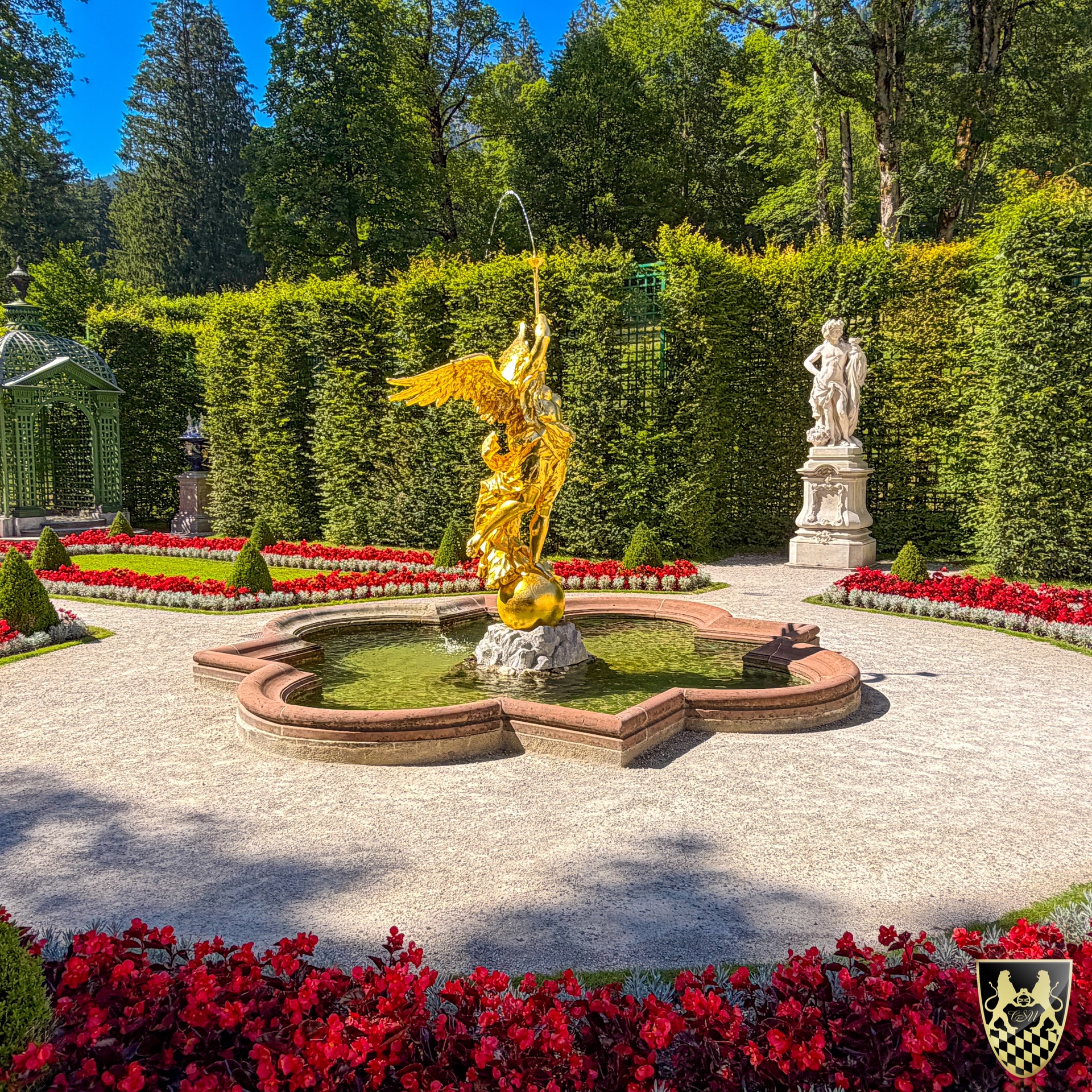 Ornate garden with golden fountain statue, hedges, and vibrant red flowers.