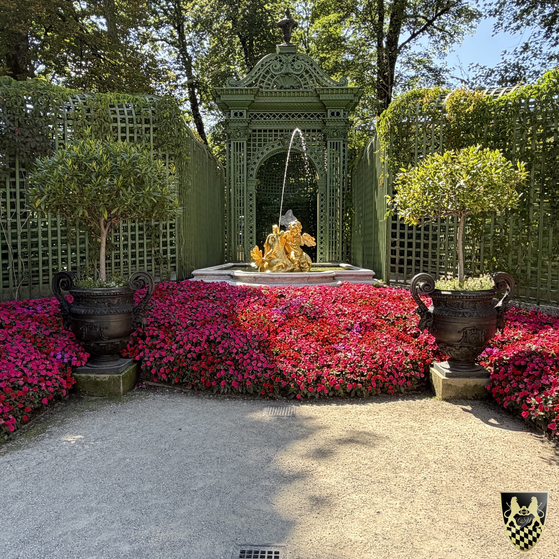 Formal garden, ornate fountain, pink flowers, green lattice, statues.