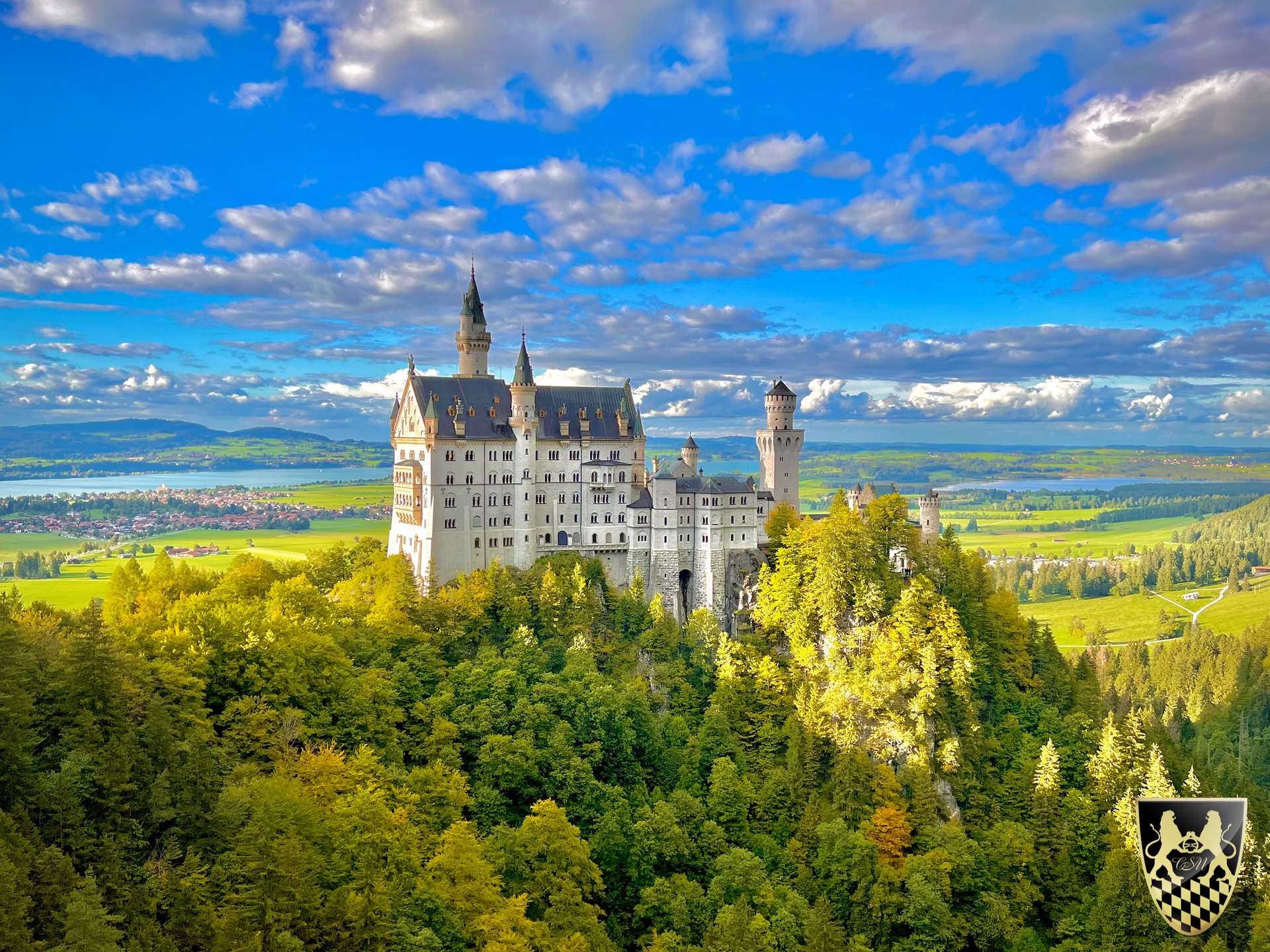 Castle on a forested hill with a background of clouds and fields.