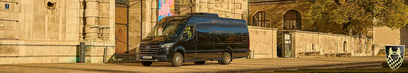 Black van parked on historic street with stone buildings and coat of arms in foreground.