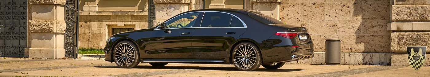 Black luxury sedan parked by ornate building in sunlight.